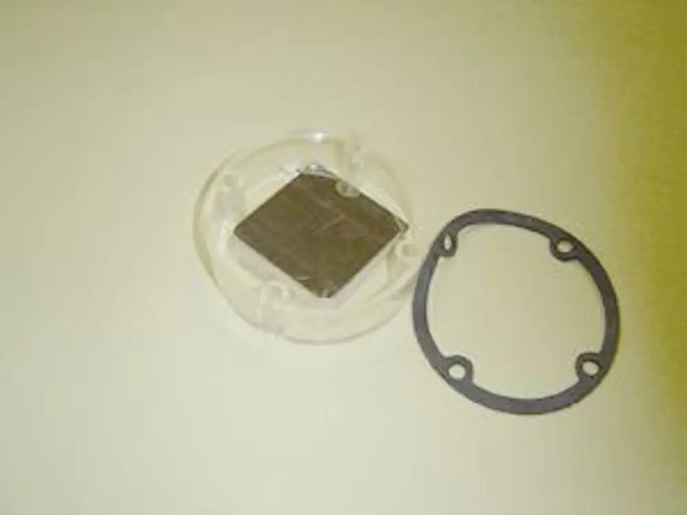 Luftklappe von Remeha bestehend aus einem rechteckigen Metallteil in einer transparenten Halterung, begleitet von einem Gummiring zur Abdichtung.